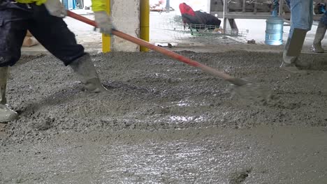 un trabajador en un sitio de construcción extendiendo la regla y nivelando un piso nuevo con una escobilla de goma