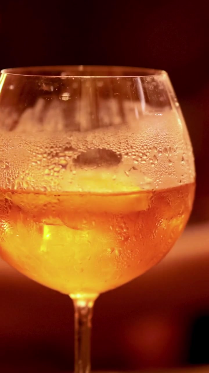 Un primo piano verticale di un bicchiere di cocktail arancione freddo con molta condensa e ghiaccio.