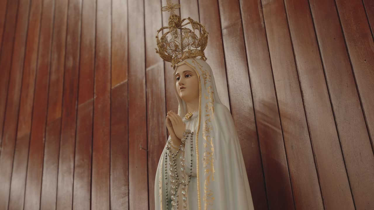 graceful statue of the Virgin Mary with a golden crown and rosary beads, placed before a wooden wall inside a Portuguese church