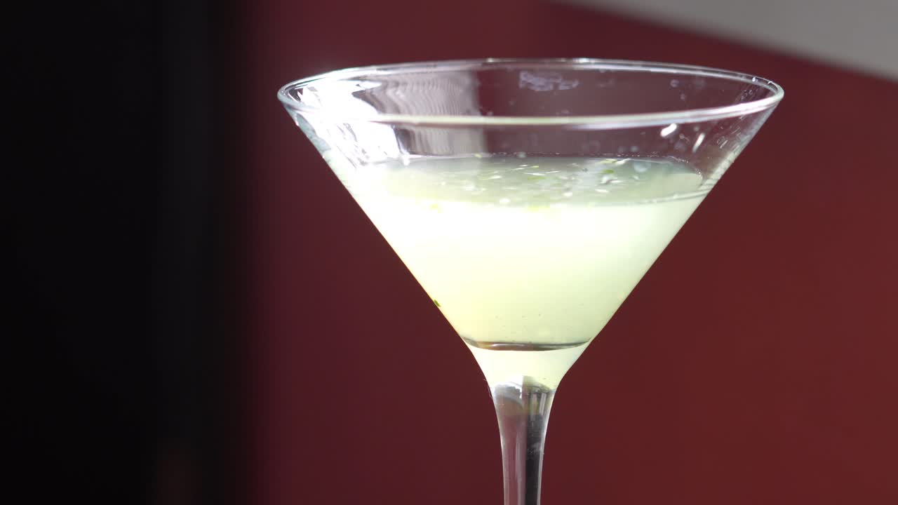 Martini Style Cocktail Beauty Shot with Lemons, Cucumber Slices and Mint Sprig on the side. Closeup Slow Pan down of Fancy, High-Class Mixed Alcoholic Drink or Beverage of Green Color