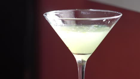 Martini Style Cocktail Beauty Shot with Lemons, Cucumber Slices and Mint Sprig on the side. Closeup Slow Pan down of Fancy, High-Class Mixed Alcoholic Drink or Beverage of Green Color
