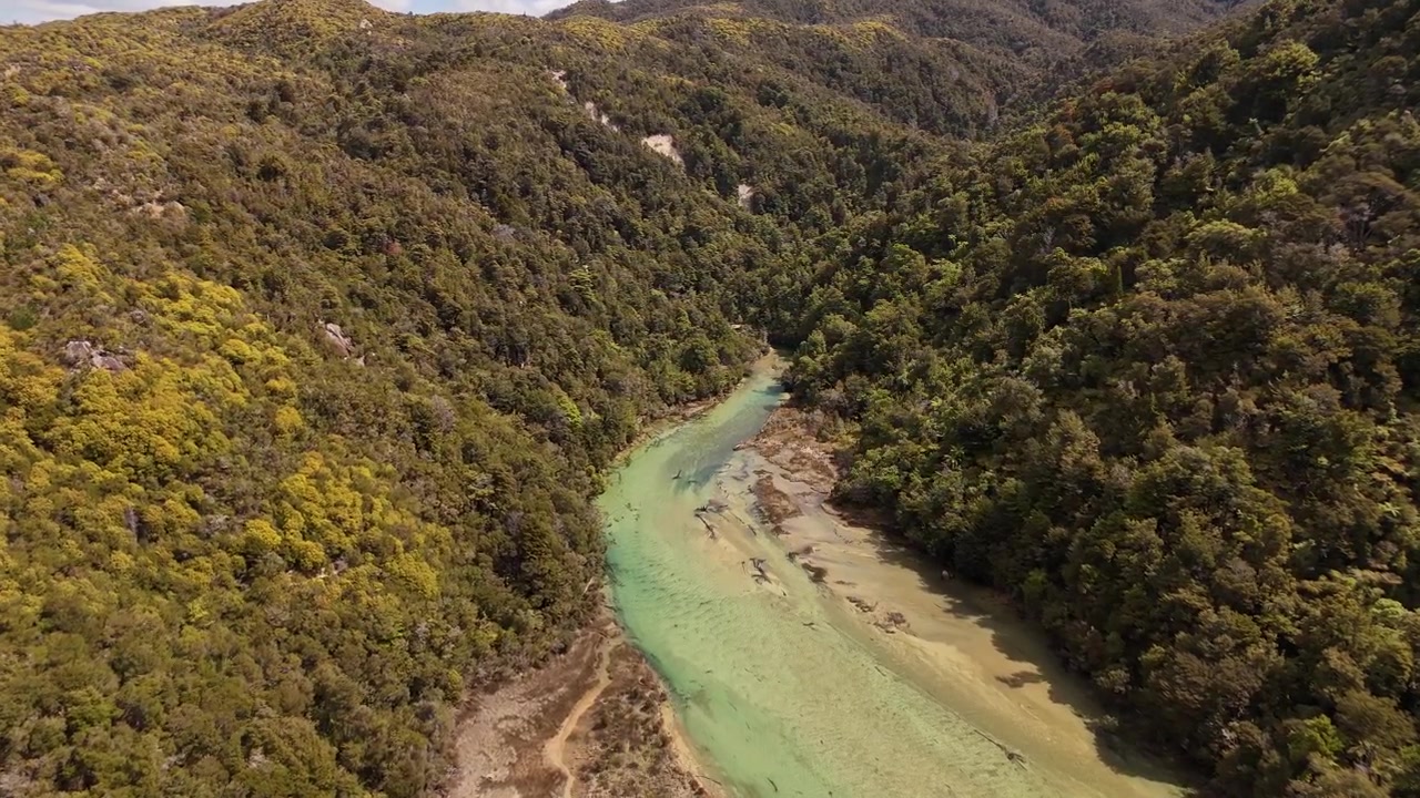 Vista aérea de um rio turquesa intocado serpenteando por um vale denso e arborizado no Parque Nacional Abel Tasman, Nova Zelândia