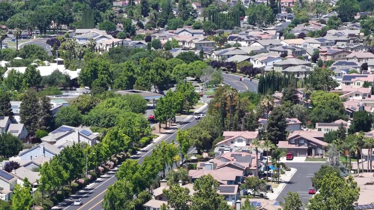 Vista aerea di un lussureggiante quartiere residenziale verde a Brentwood, California, che mostra case con pannelli solari sui tetti, strade tranquille e alberi abbondanti in una soleggiata giornata estiva