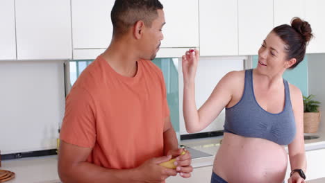 pregnant woman feeding partner banana in modern kitchen, sharing moment