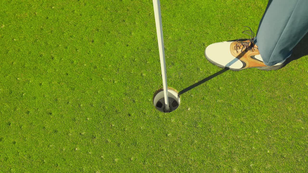 Overhead view of a golf ball rolling and dropping into a hole on a putting green