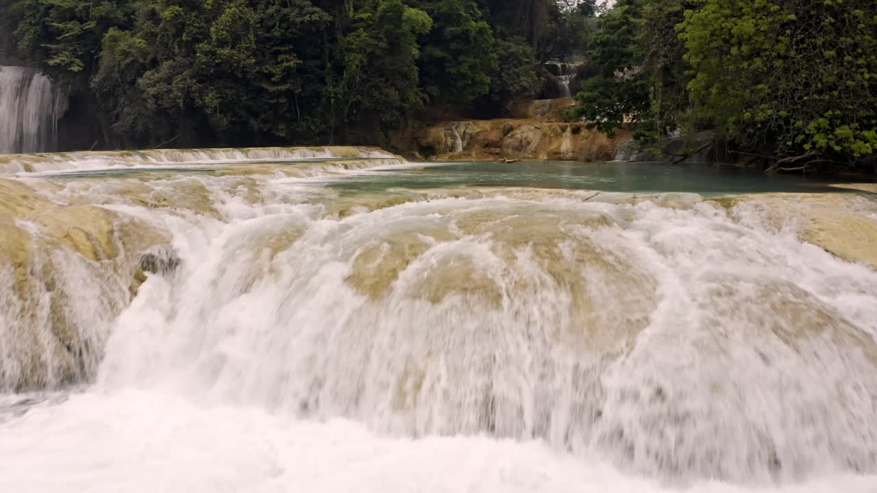 An aerial drone shot of man swimming in the Cascadas de Agua Azul in Chiapas, México, showing the brilliant turquoise water of a natural swimming pool