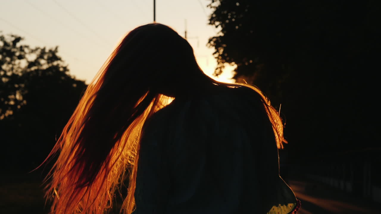 긴 머리를 가진 소녀의 실루엣이 머리를 흔들고 햇볕에 머리를 가지고 논다