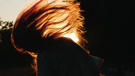 silhouette of a girl with long hair shakes his head and plays with his hair in the sun