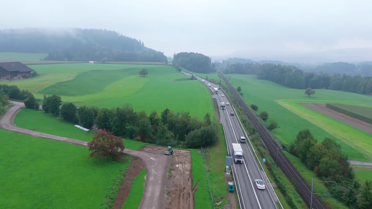 Morning traffic flows beside a rural railway through green fields, Aerial