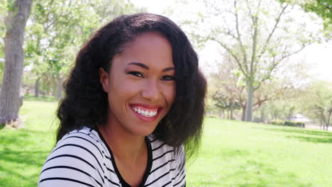 Outdoor-Head-And-Shoulders-Portrait-Of-Smiling-Young-Woman-In-Park