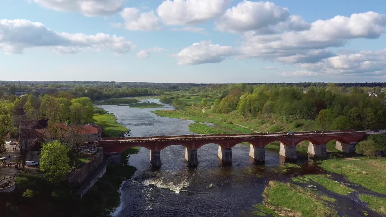 clip aéreo 4k, volando sobre la pequeña ciudad de kuldiga letonia, puente de ladrillo rojo sobre el río venta, amplia cascada