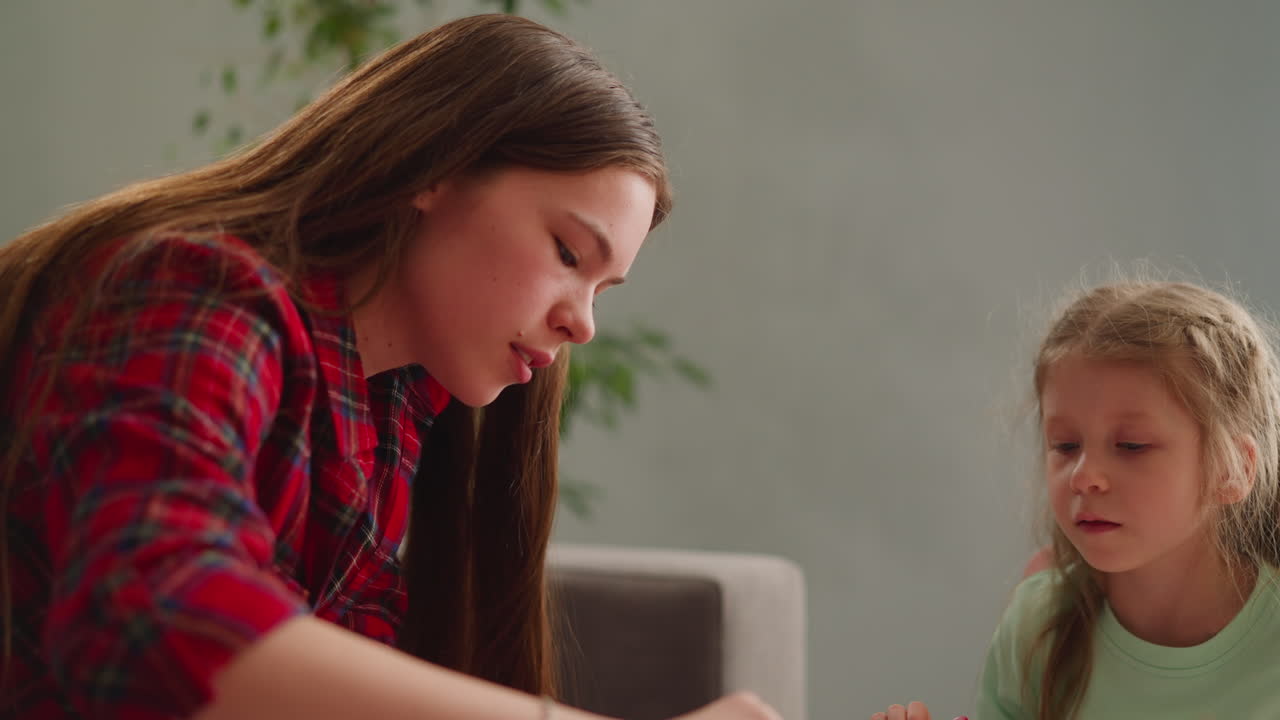 концентрированная девушка смотрит на длинноволосую сестру, смешивающую цвета