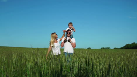 the happy family runs and smiles in the field with their son laughing and holding hands. son sitting on the lash