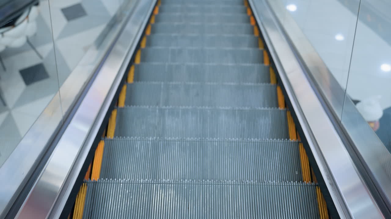 Upward-moving escalator with sleek glass frame and reflections along the border in a modern shopping mall, smooth metal steps, polished railing, and dynamic perspective