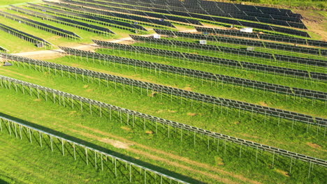 expansive rows of solar panels in green field in establishing drone shot