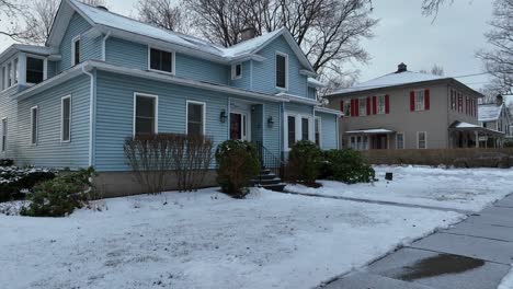 Low-aerial-glide-towards-blue-house-covered-in-snow-on-winter-day