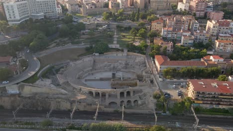 Ein-Faszinierender,-Langsamer-Drohnenclip,-Der-Das-Antike-Römische-Kolosseum-Inmitten-Der-Zersiedelung-Von-Tarragona,-Spanien,-Einfängt