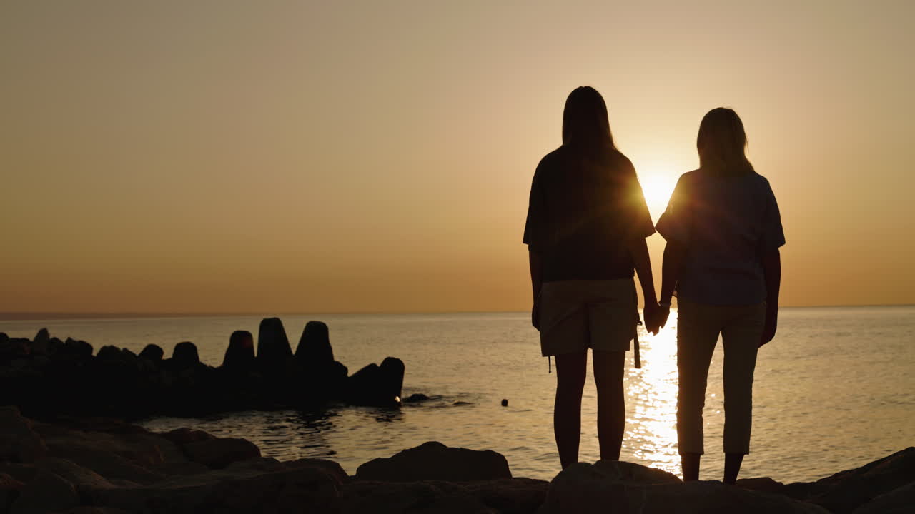 Two women holding hands at sunset by the beach