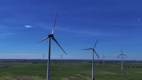 Wind-turbines-spinning-on-a-sunny-day-in-a-vast-green-field,-clear-blue-sky-overhead