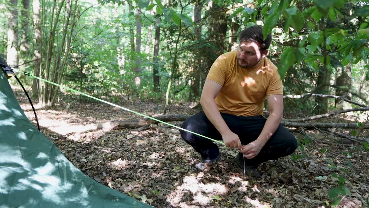 젊은 남자는 삼림 지대 지역에서 텐트 끈을 사용하고, 휴대용 보기