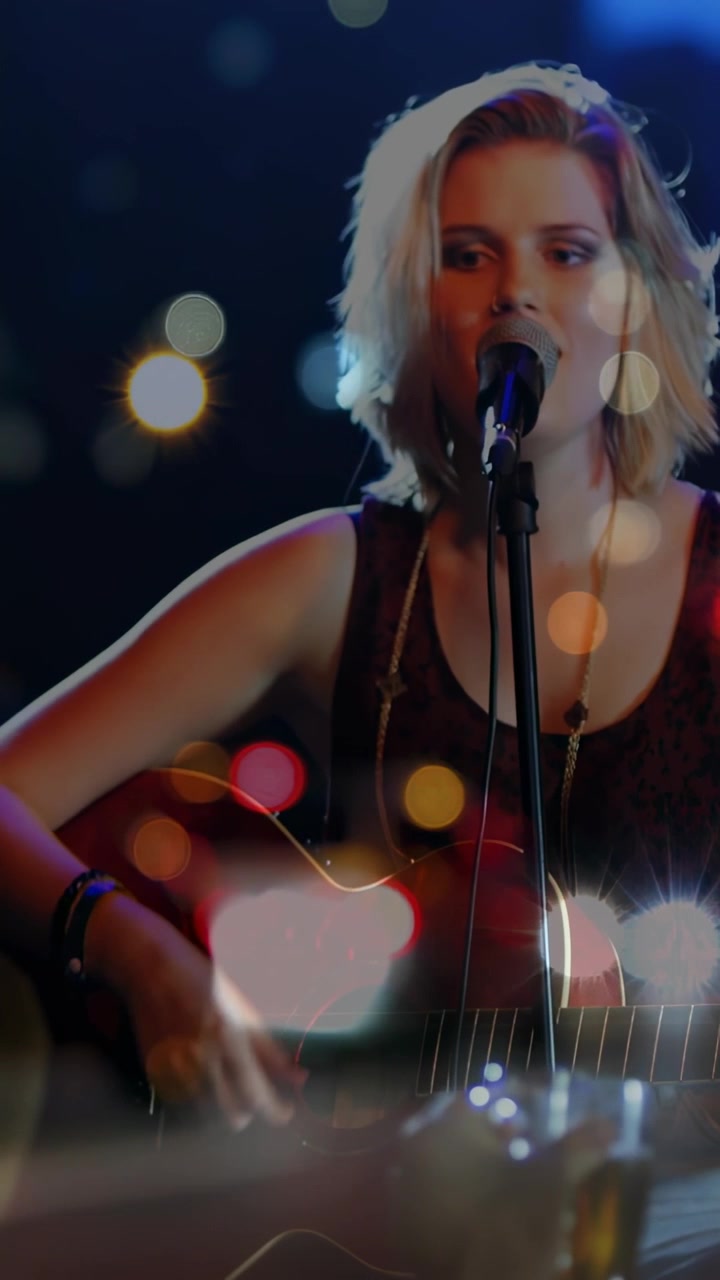 Vertical video: Focus shift revealing singer strumming guitar and singing for music crowd