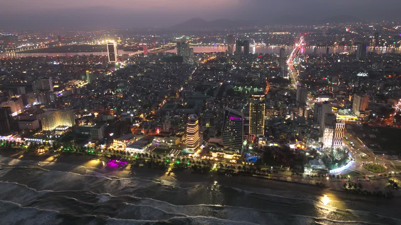 Luftfoto i fugleperspektiv af den moderne by Da Nang om natten med oplyst skyline og Han River Bridge i centrum, drone rejsedestination