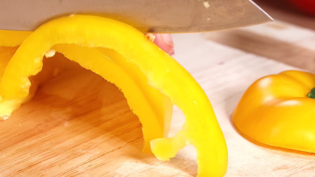 Close-up of hands slicing yellow bell peppers into strips on a wooden board.