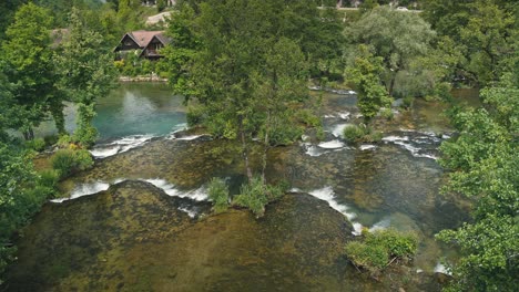 River-with-small-waterfalls-flowing-through-lush-greenery-and-traditional-houses-in-Rastoke,-Croatia