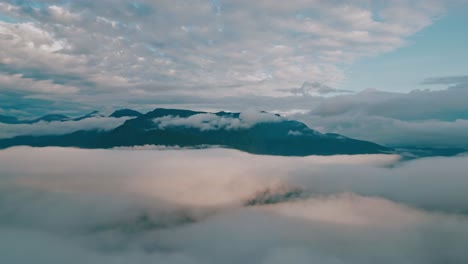 Soar-effortlessly-above-the-clouds-in-this-mesmerizing-drone-footage,-with-majestic-mountain-peaks-piercing-the-sky-behind,-creating-a-spectacular-setting-for-the-lush-Yungas-cloud-forest-beneath