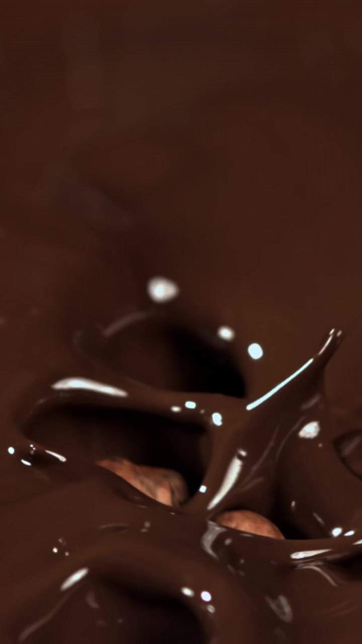 Nocciole che cadono e si tuffano nel cioccolato fuso al rallentatore
