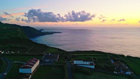 Sonnenuntergang-über-Einem-Küstendorf-Mit-Sanften-Hügeln-Und-Dem-Meer-Im-Hintergrund