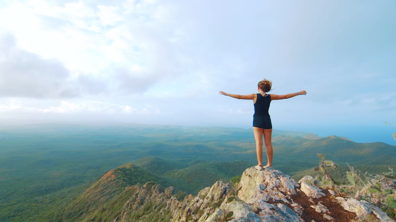 mujer joven con los brazos levantados en el pico de la montaña con vistas al paisaje de la selva