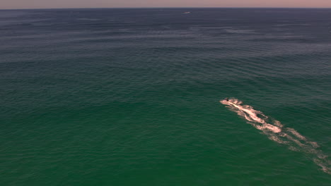 vista aérea revelada de un dron rastreando una moto acuática mientras se adentra en el océano en un hermoso día tranquilo en el popular mirador marítimo de spit gold coast, queensland, australia.