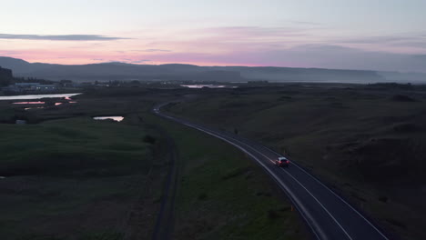 Drone-view-of-highway-car-peacefully-driving-at-evening.-Aerial-view-of-ring-road-in-Iceland-with-fast-driving-car-at-sunset