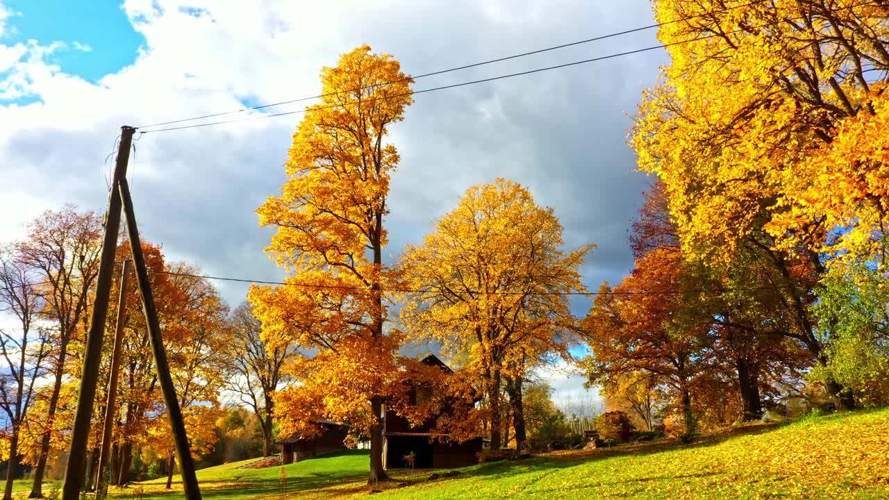 Herbstliche Landschaft mit Holzhäusern und Stromleitungen unter dramatischem Himmel