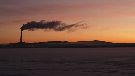 silhouette of smoking power plant in morning sun across frozen lake