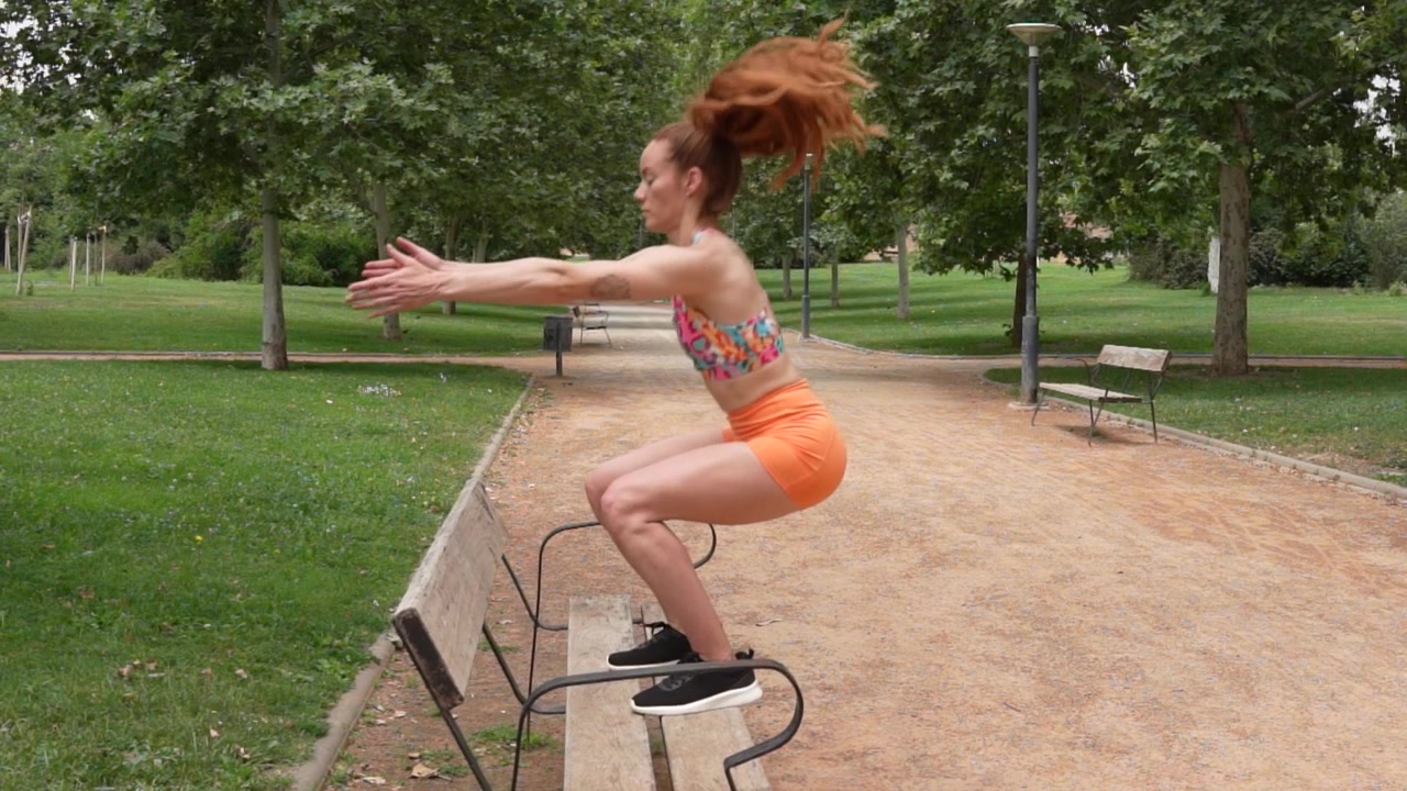 Allenamento fitness all'aperto con una donna che esegue step-up e salti su una panchina del parco.