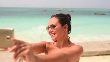 Hand-held-shot-of-brunette-girl-with-sunglasses-taking-selfie-on-Zanzibar-beach,-Tanzania