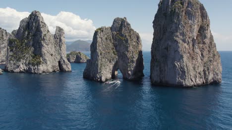 aerial of yachts boating under the natural arch of the faraglioni sea stacks on coast of capri island, italy