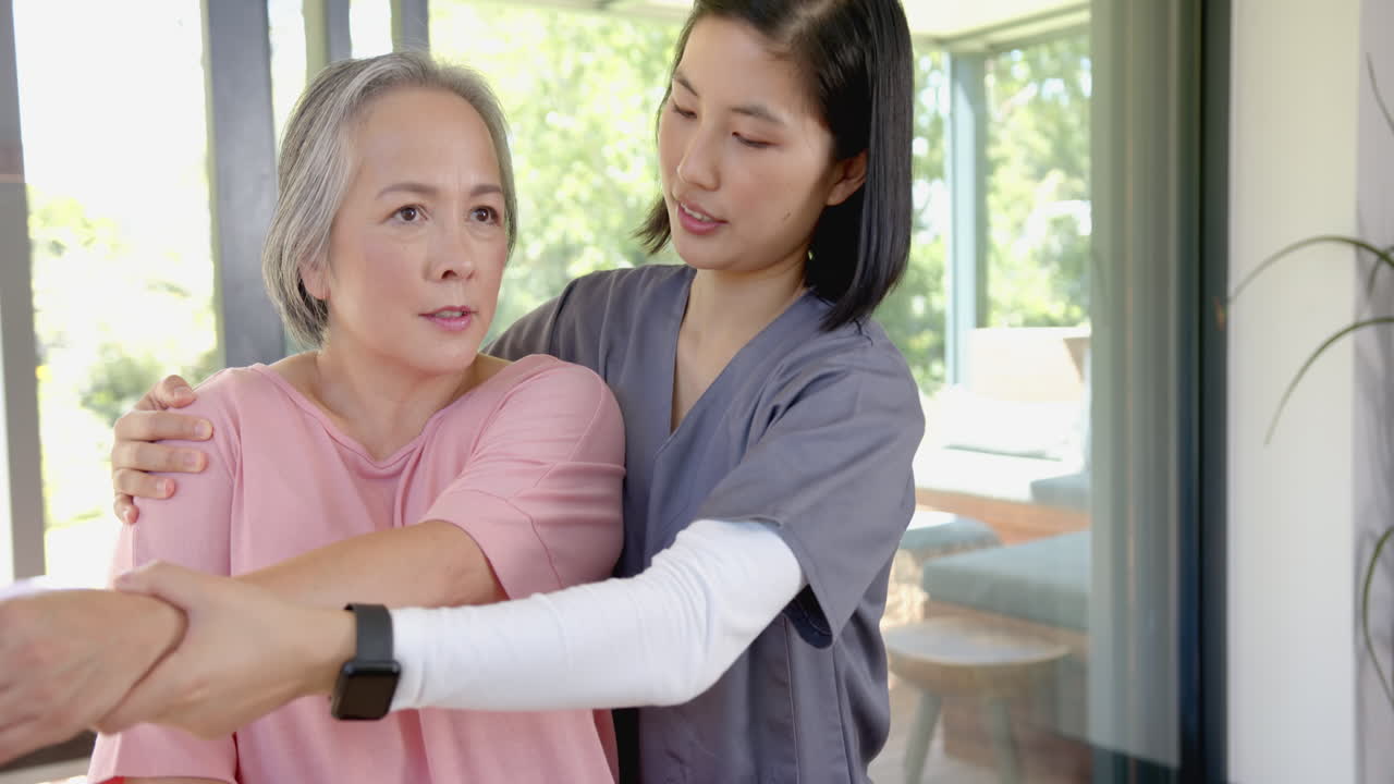 Physical therapist assisting senior asian woman with arm exercises at home
