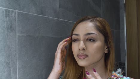 close up of young asian indian female checking her skin in mirror in bathroom with both hands