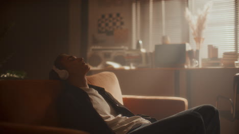 relaxed man in headphones leaning back on couch, enjoying music in sunlit room