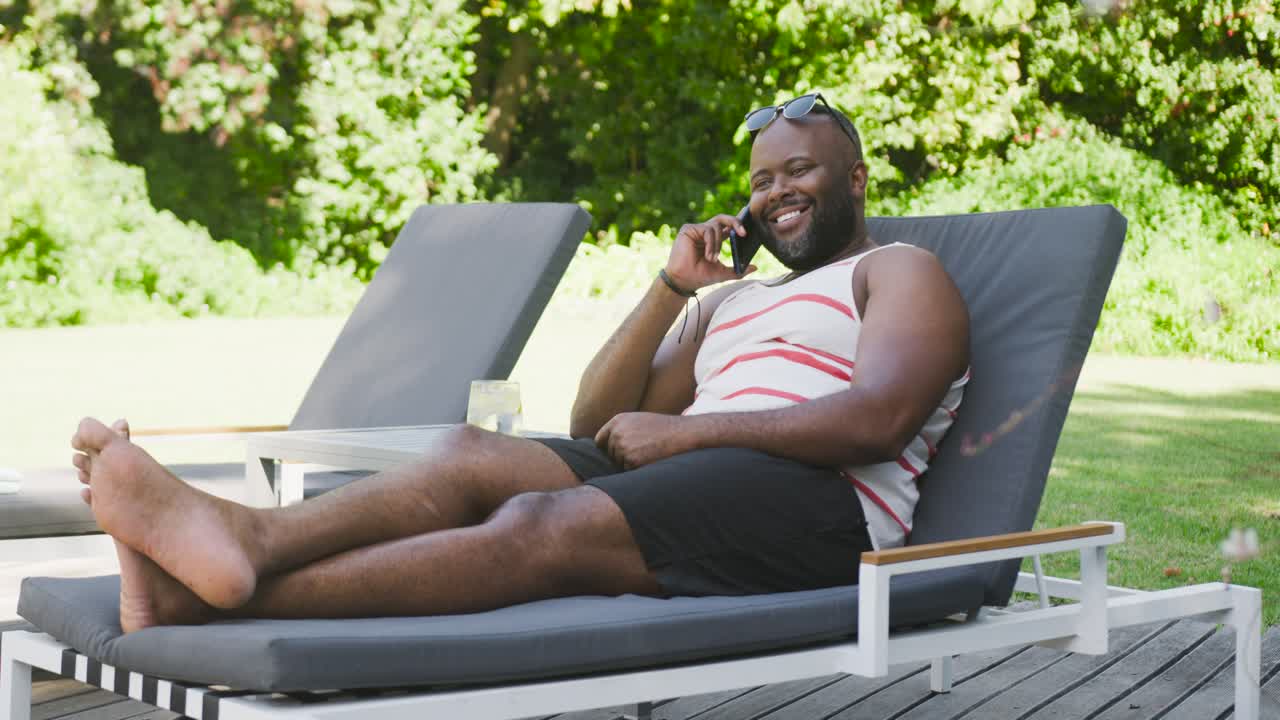 Telefonen ringer, afroamerikansk mand i liggestol holder smartphone, smiler og griner derefter