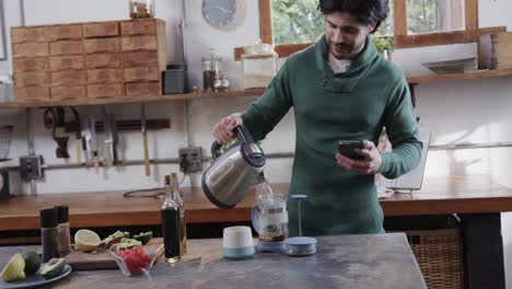 Hombre-Caucásico-Haciendo-Café-Y-Usando-Un-Teléfono-Inteligente-En-La-Cocina,-Cámara-Lenta