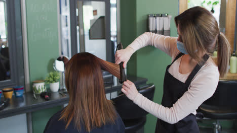 Friseurin-Mit-Gesichtsmaske-Glättet-Haare-Einer-Kundin-Im-Friseursalon