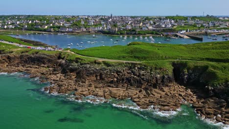 rocky coast, le conquet harbor, kermorvan peninsula, boats in water, and coastal town, brittany, france. aerial drone forward
