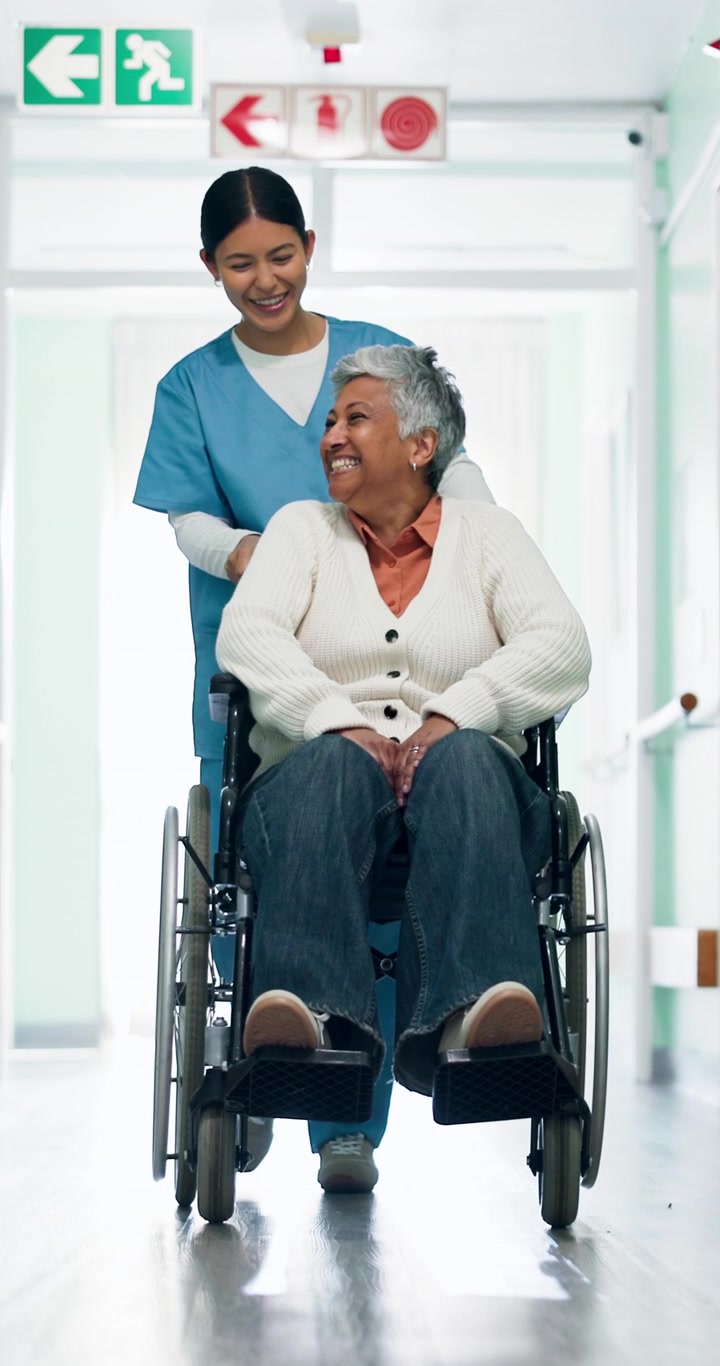 Nurse Pushing Senior Woman in Wheelchair Through Hospital Corridor