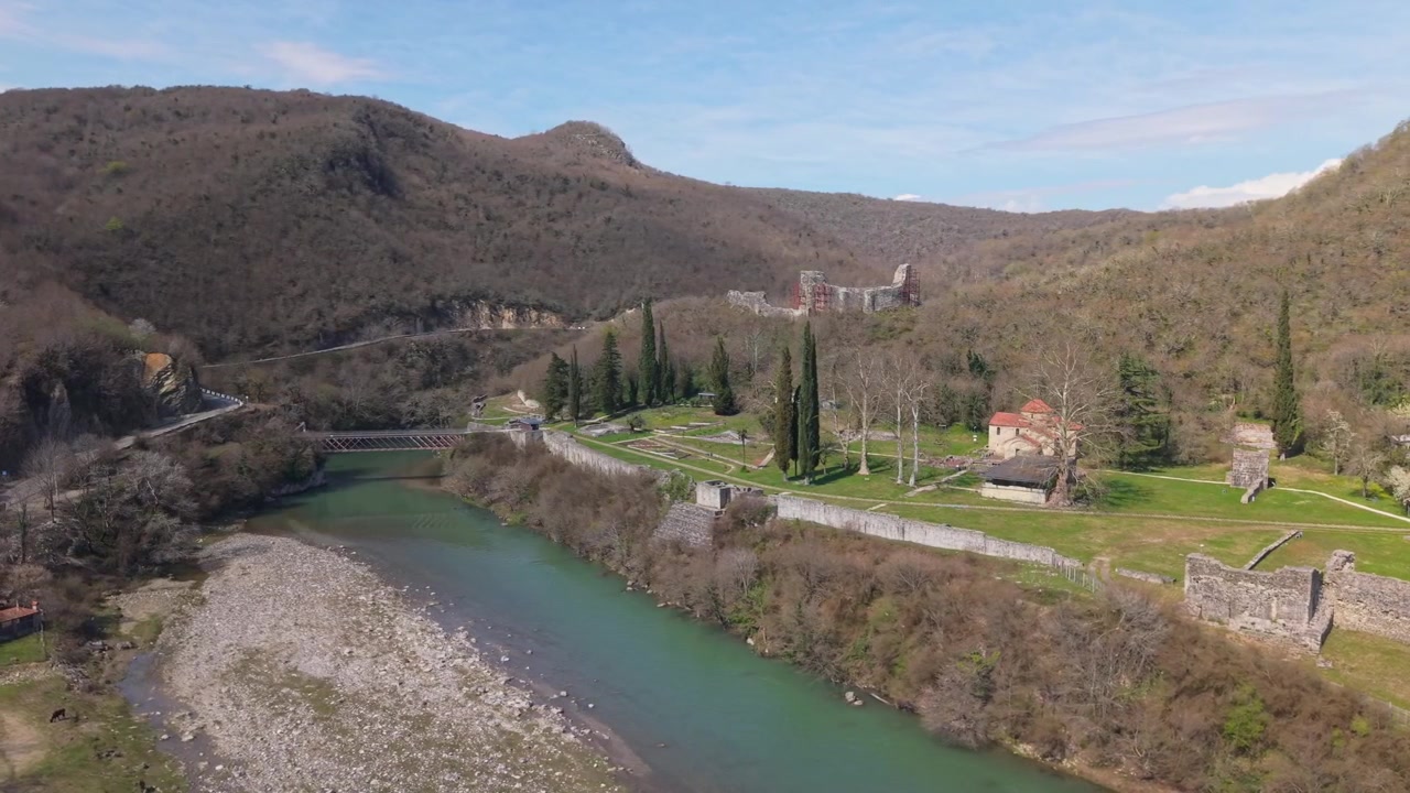 Orbita di drone aereo che svela la storica Fortezza di Nokalakevi nella Georgia occidentale, circondata da una vivace vegetazione primaverile, dolci colline lussureggianti e antiche rovine in pietra nel Samegrelo.