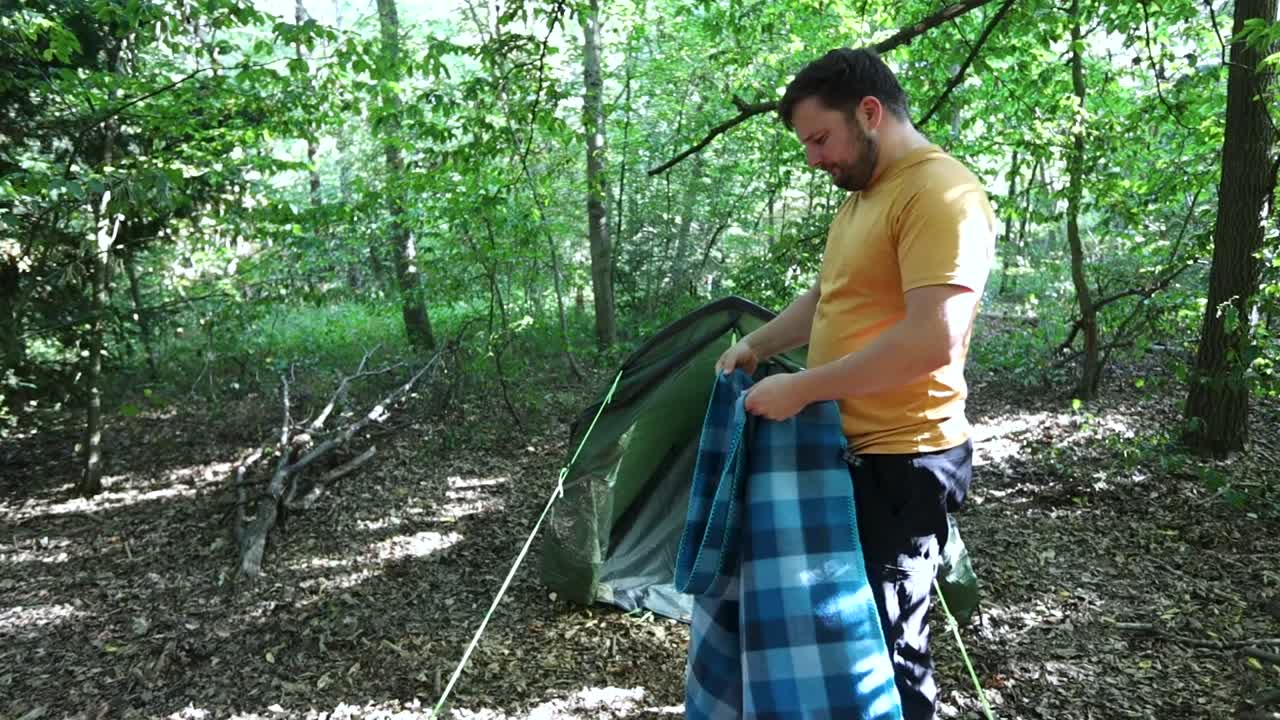 persona temblando para limpiar la manta en el camping del bosque, vista en movimiento