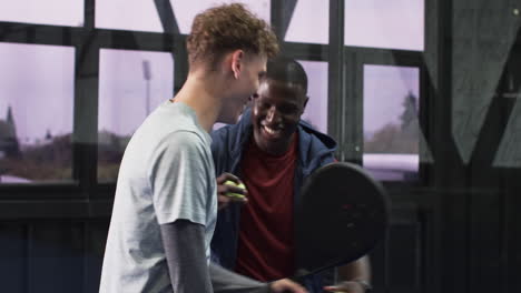 two diverse men playing padel tennis indoors, smiling and enjoying game, at indoor court